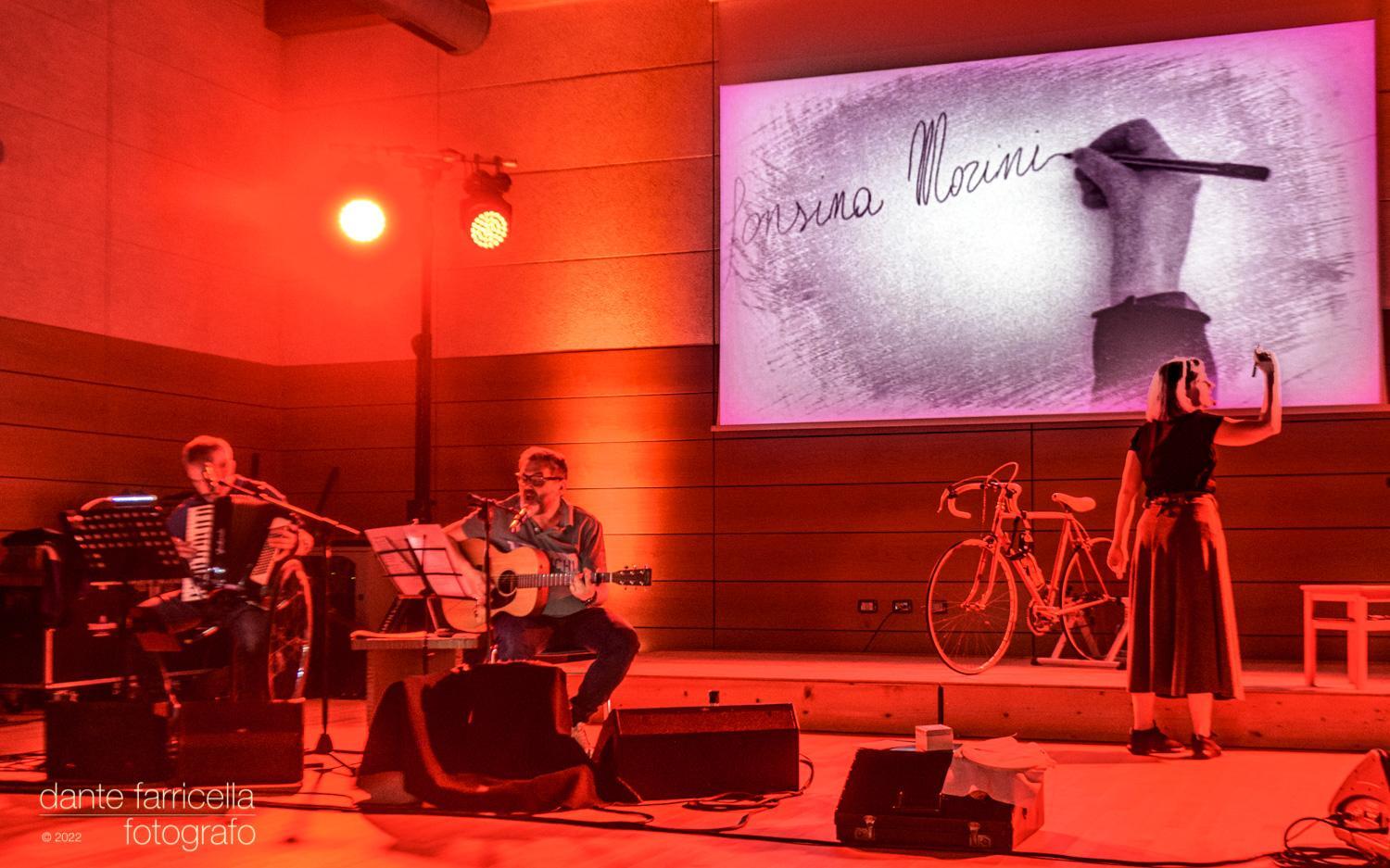 Maria Giulia Campioli e i musicisti in scena, con la firma di Alfonsina Morini proiettata sullo schermo.